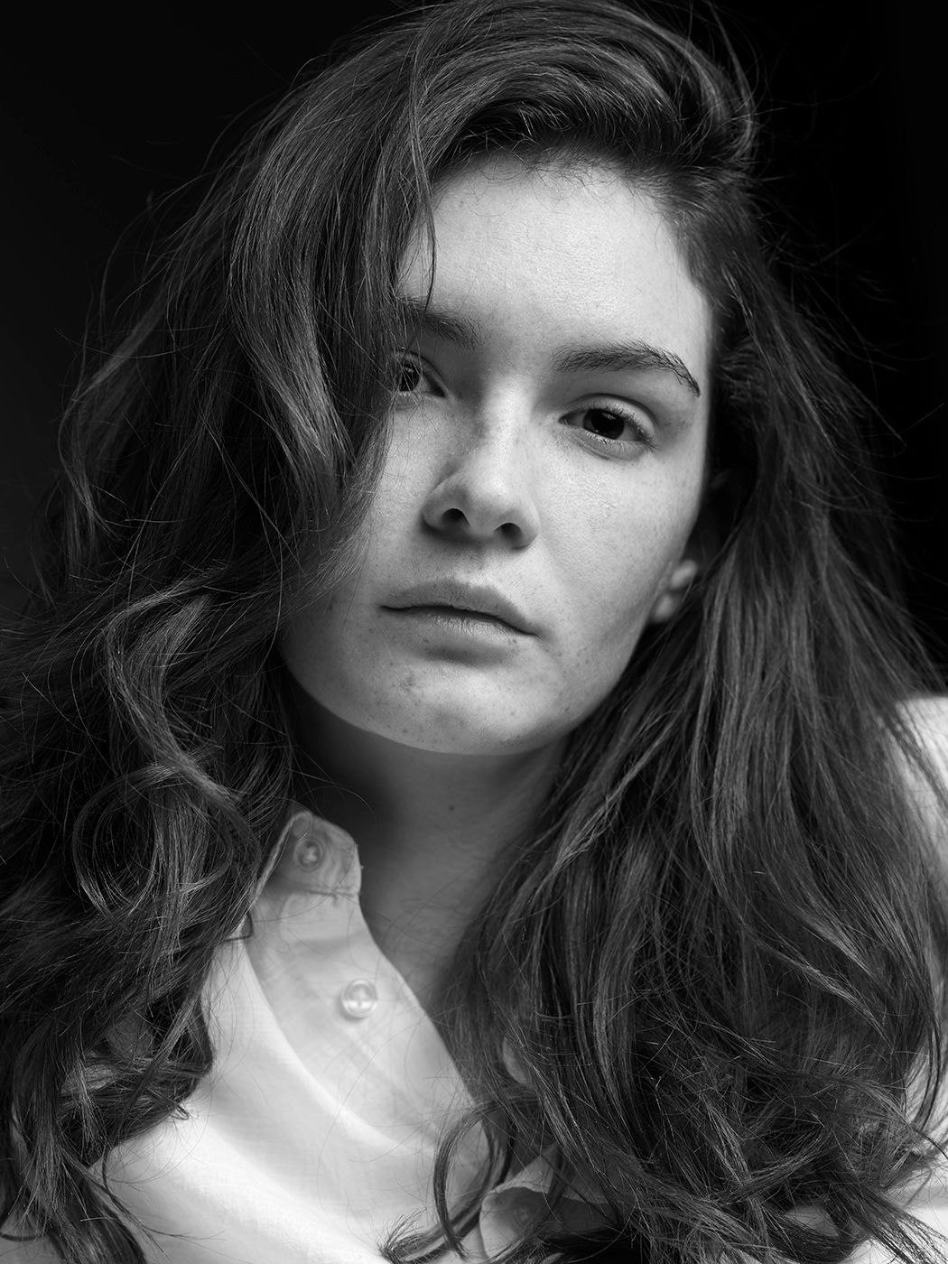Black and white portrait of a young woman with long wavy hair wearing a white collared shirt.