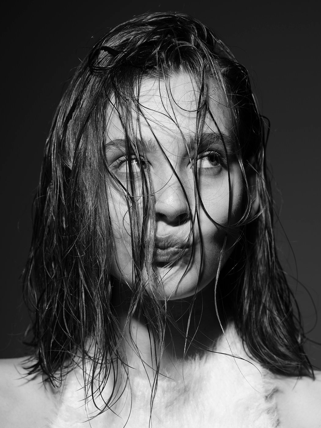 Black and white portrait of a young woman with wet hair blowing across her face, making a pouty expression.