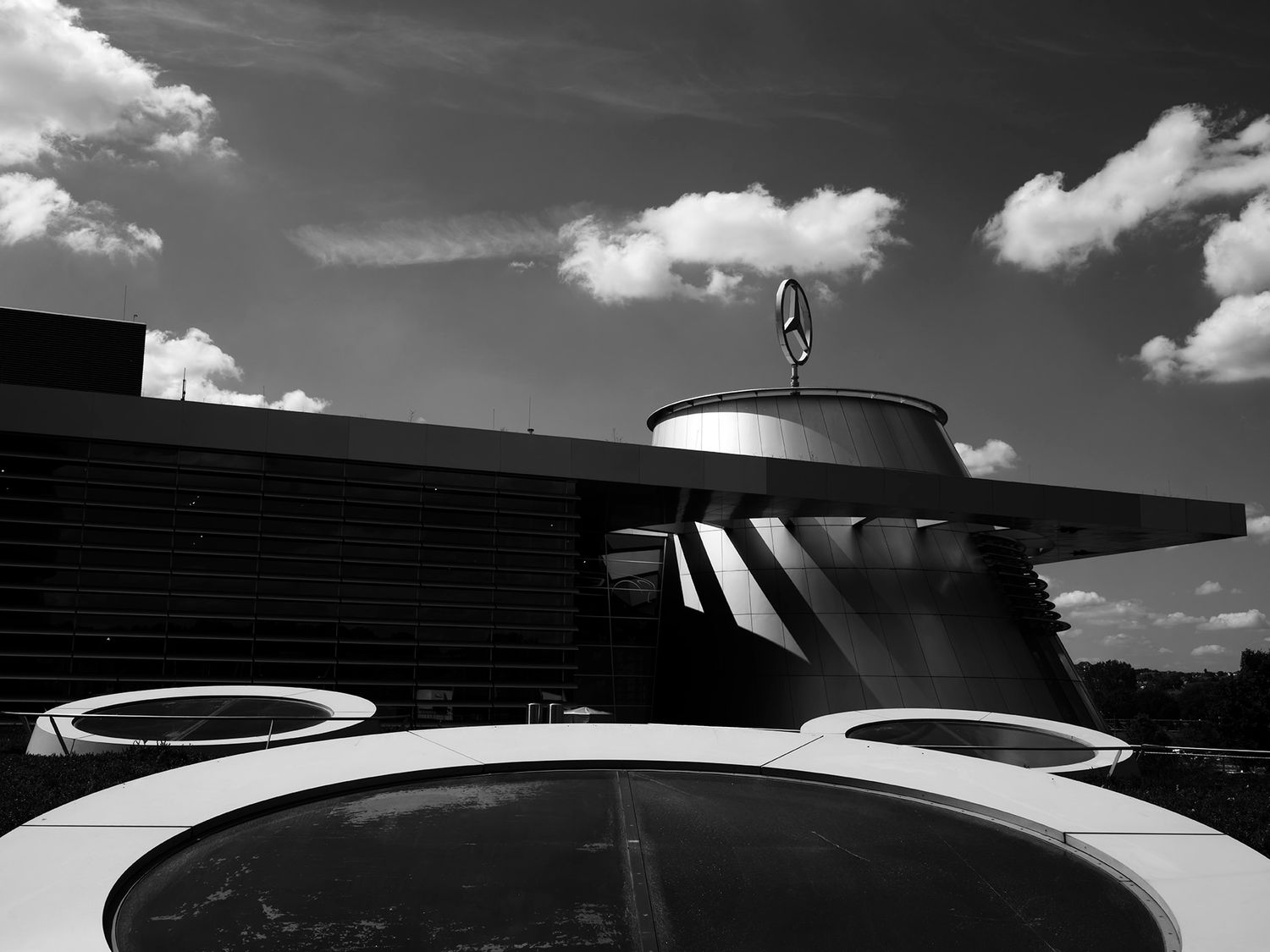Black and white photo of a Mercedes-Benz dealership rooftop with iconic star logo against a cloudy sky.