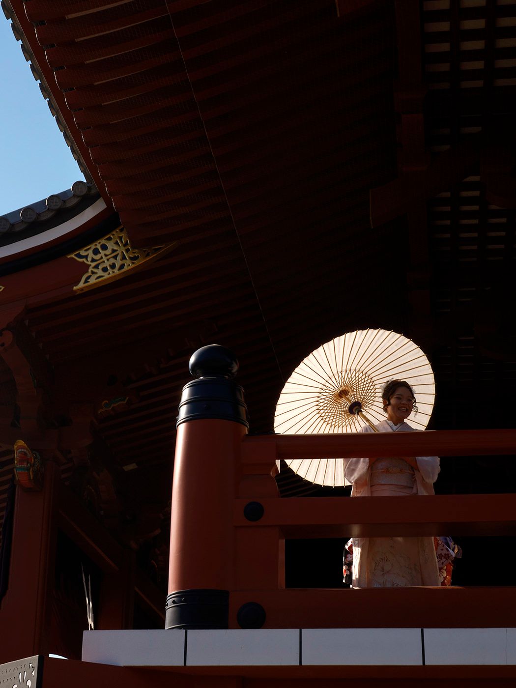 Woman in traditional Japanese kimono holding a white wagasa parasol on a vermillion temple balcony.