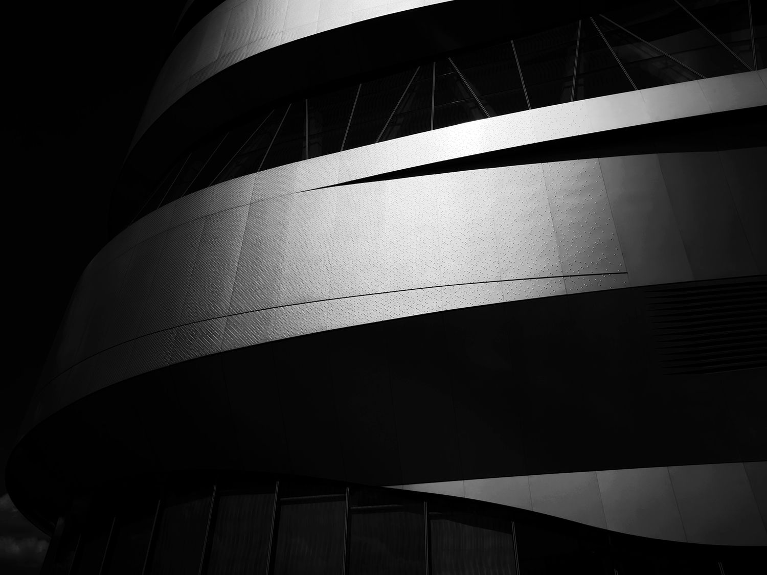 Black and white architectural photo of a curved modern building facade with dramatic lighting and geometric lines.