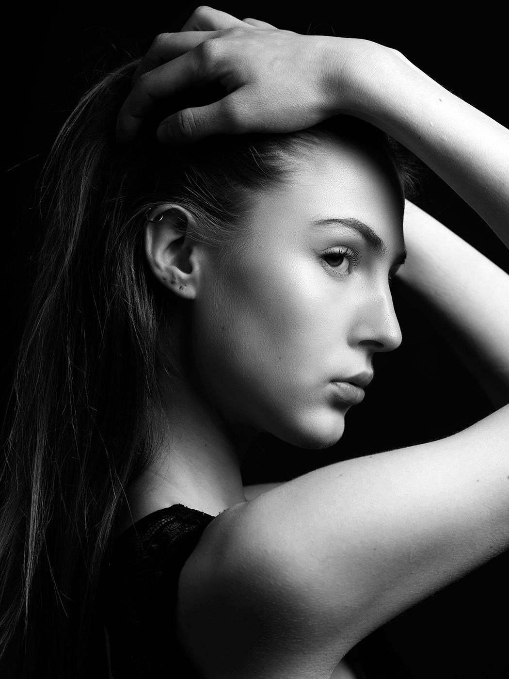 Black and white portrait of a young woman with long hair, hands raised gracefully near her head, dramatic lighting.