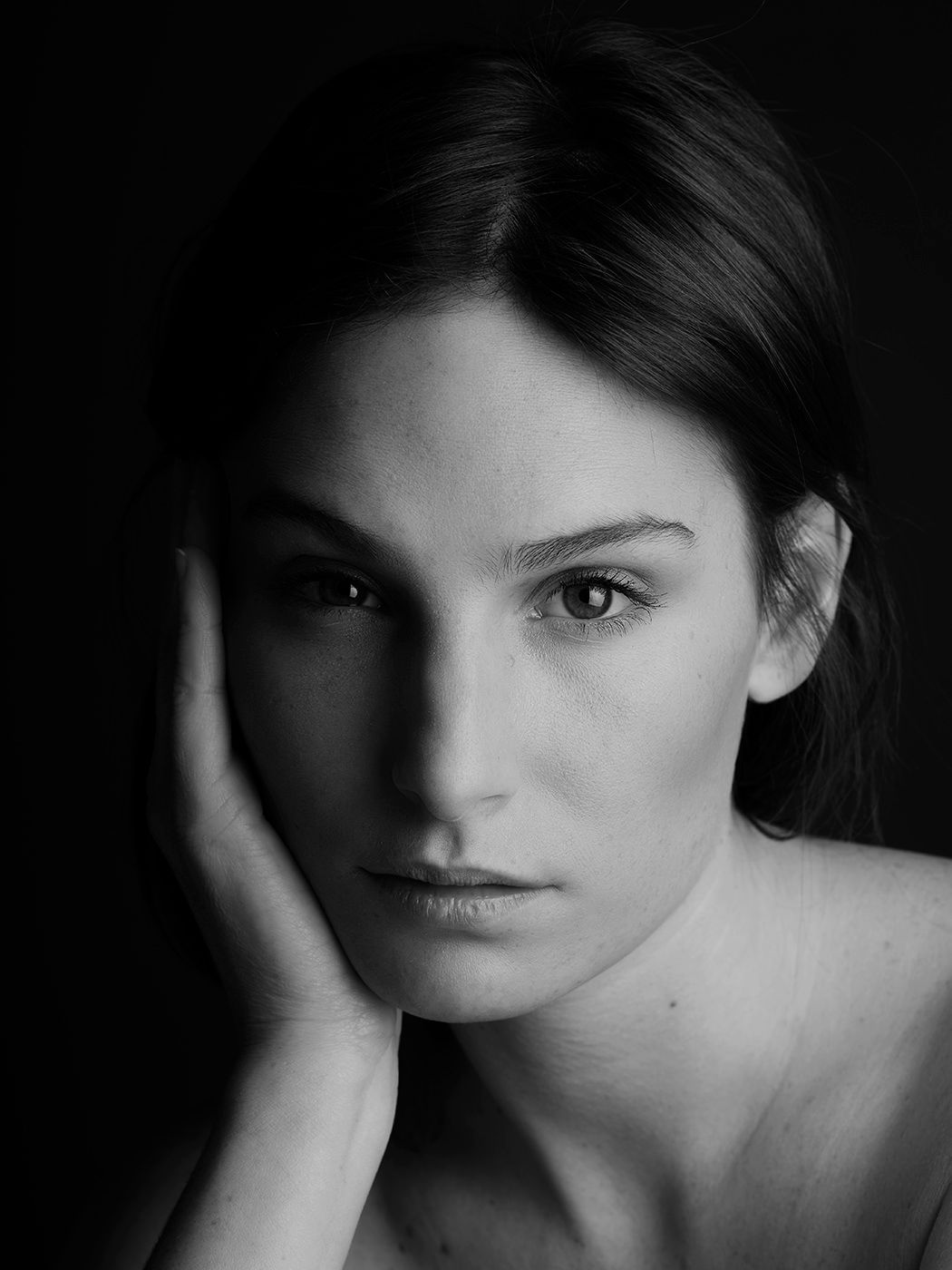 Black and white portrait of a young woman resting her cheek on her hand, gazing thoughtfully at the camera.