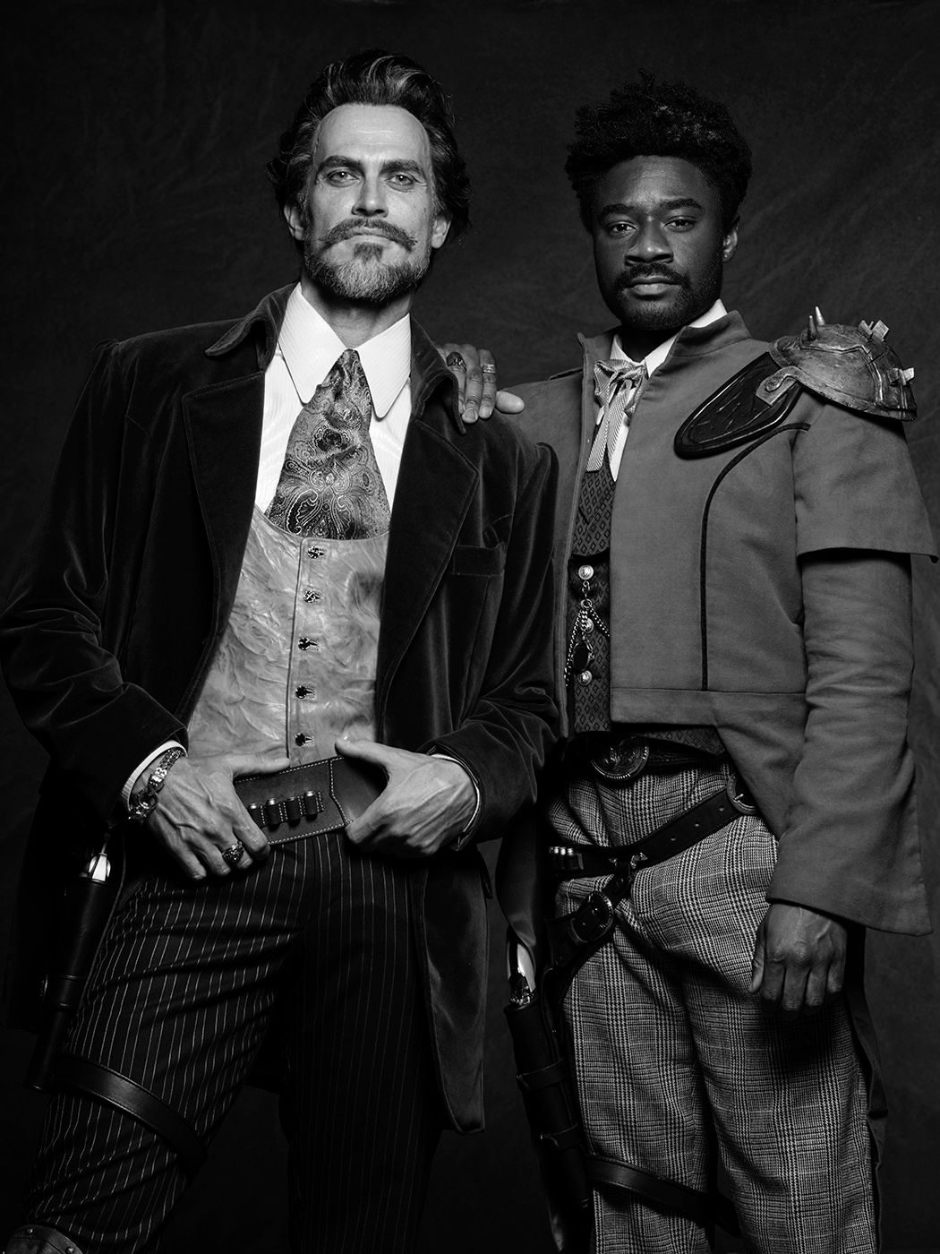 Two men in vintage Victorian-style suits pose together in a black and white portrait photo.