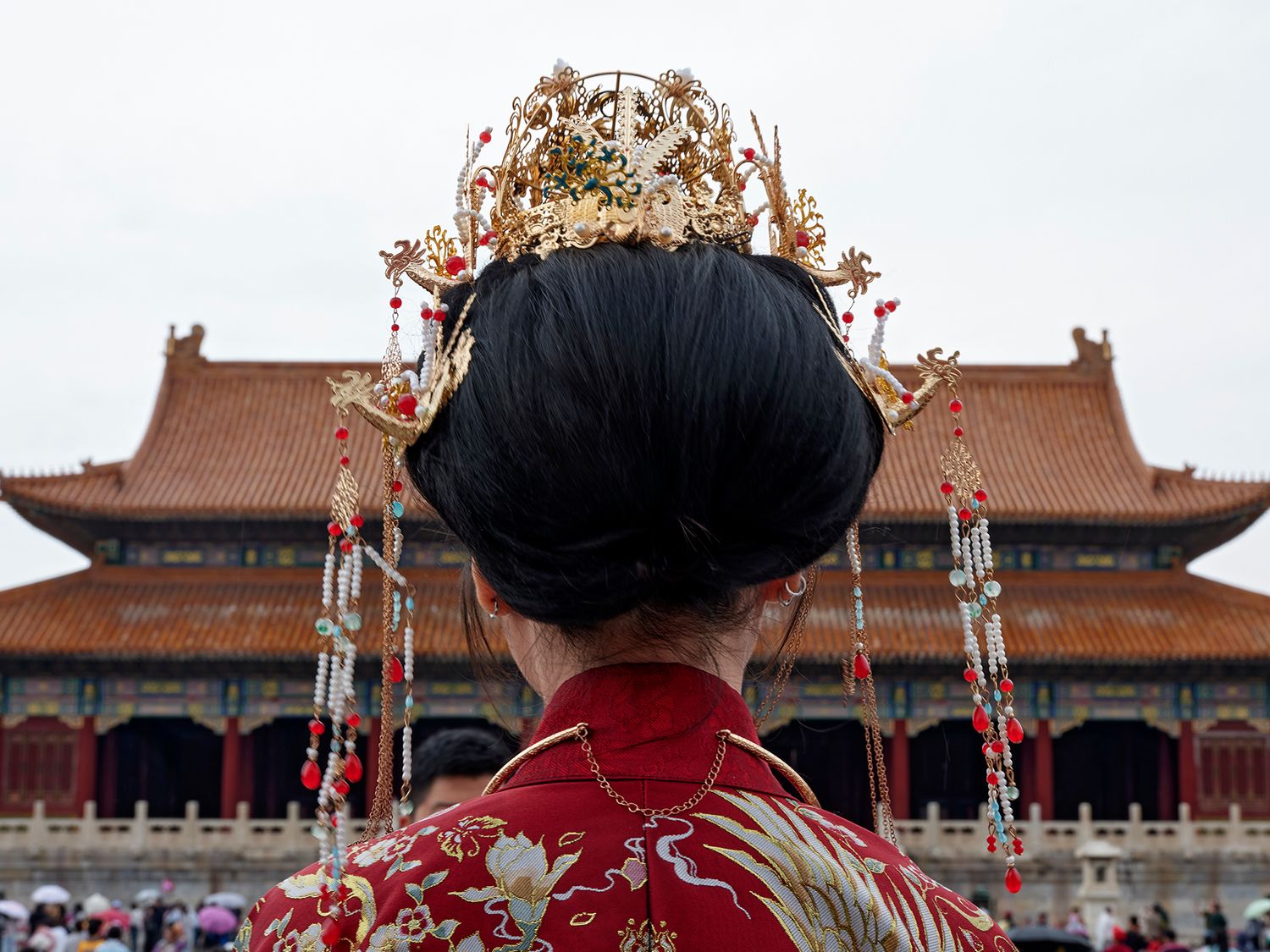 Woman in traditional Chinese empress costume with ornate gold crown stands before the Forbidden City in Beijing.