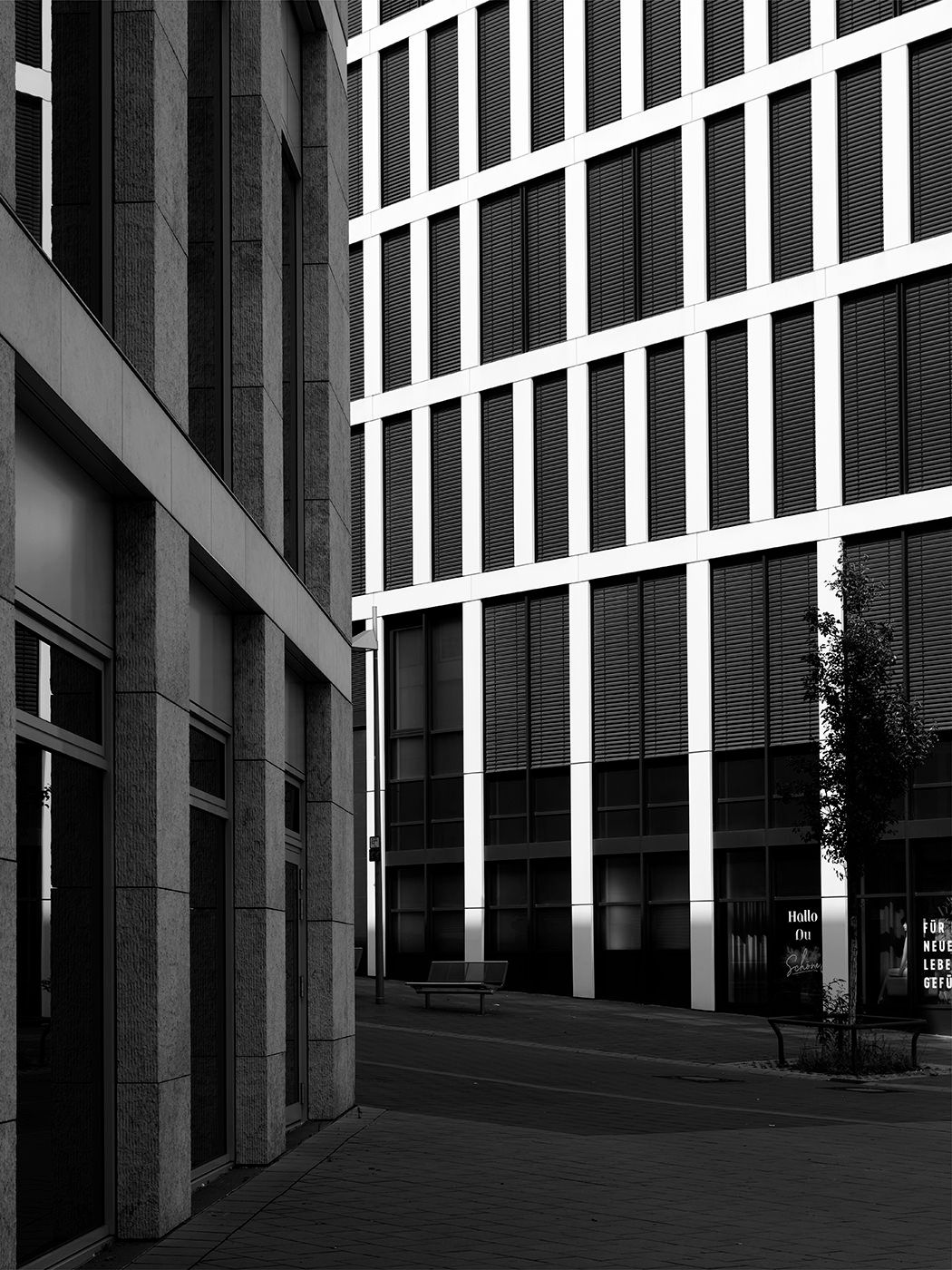 Black and white urban architecture photo showing modern office buildings with grid windows and a narrow alley between structures.