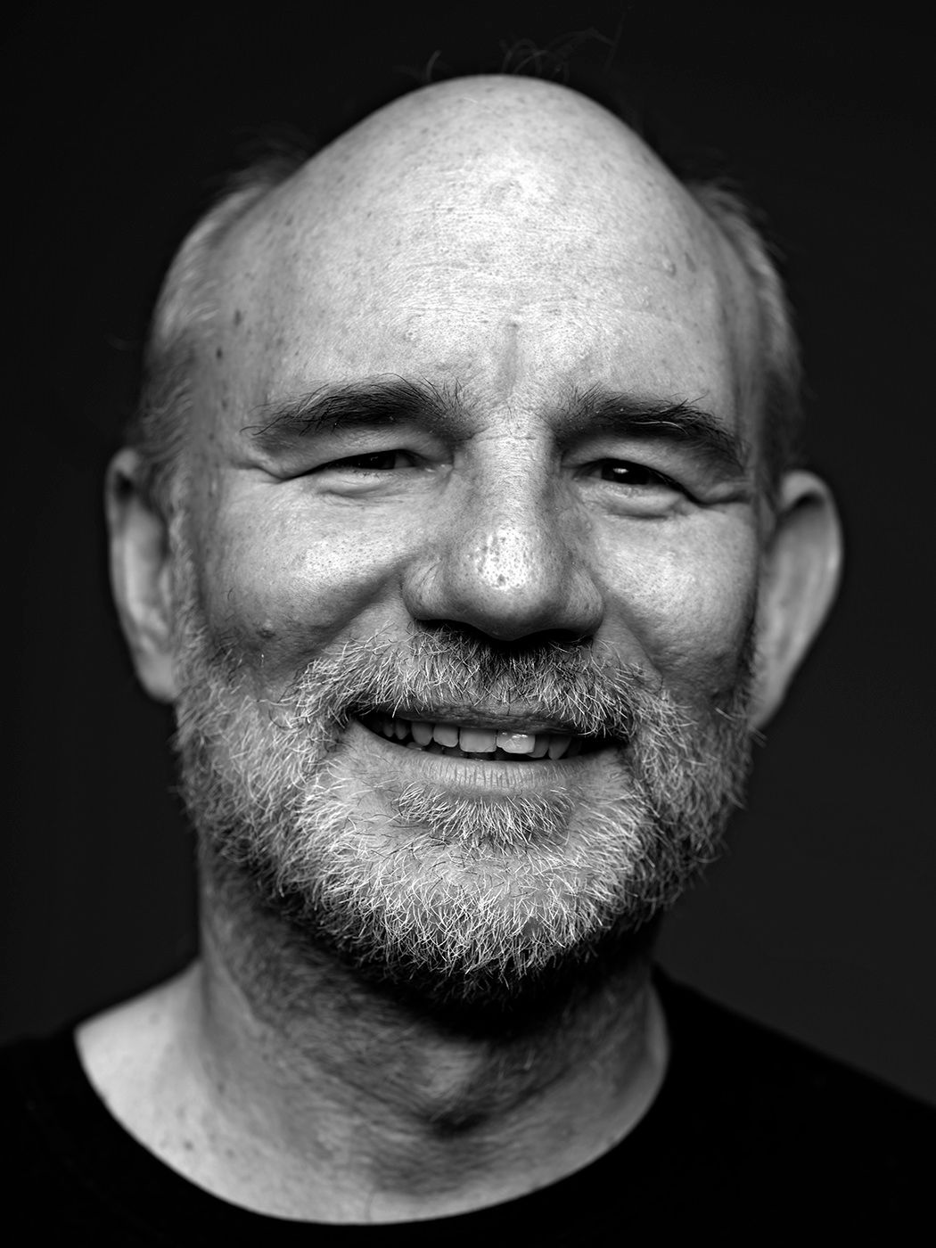 Black and white portrait of a smiling bald older man with a beard, captured in a studio setting. Juhász Gábor