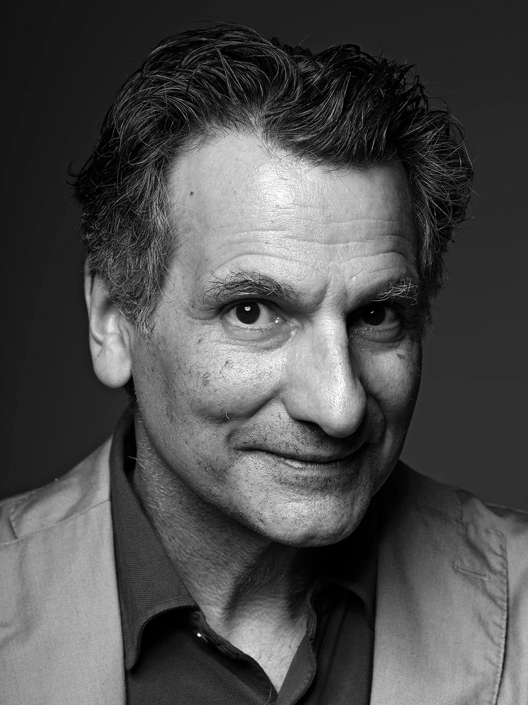 Black and white portrait of a middle-aged man with curly hair, smiling subtly in a professional headshot photo. John Patitucci