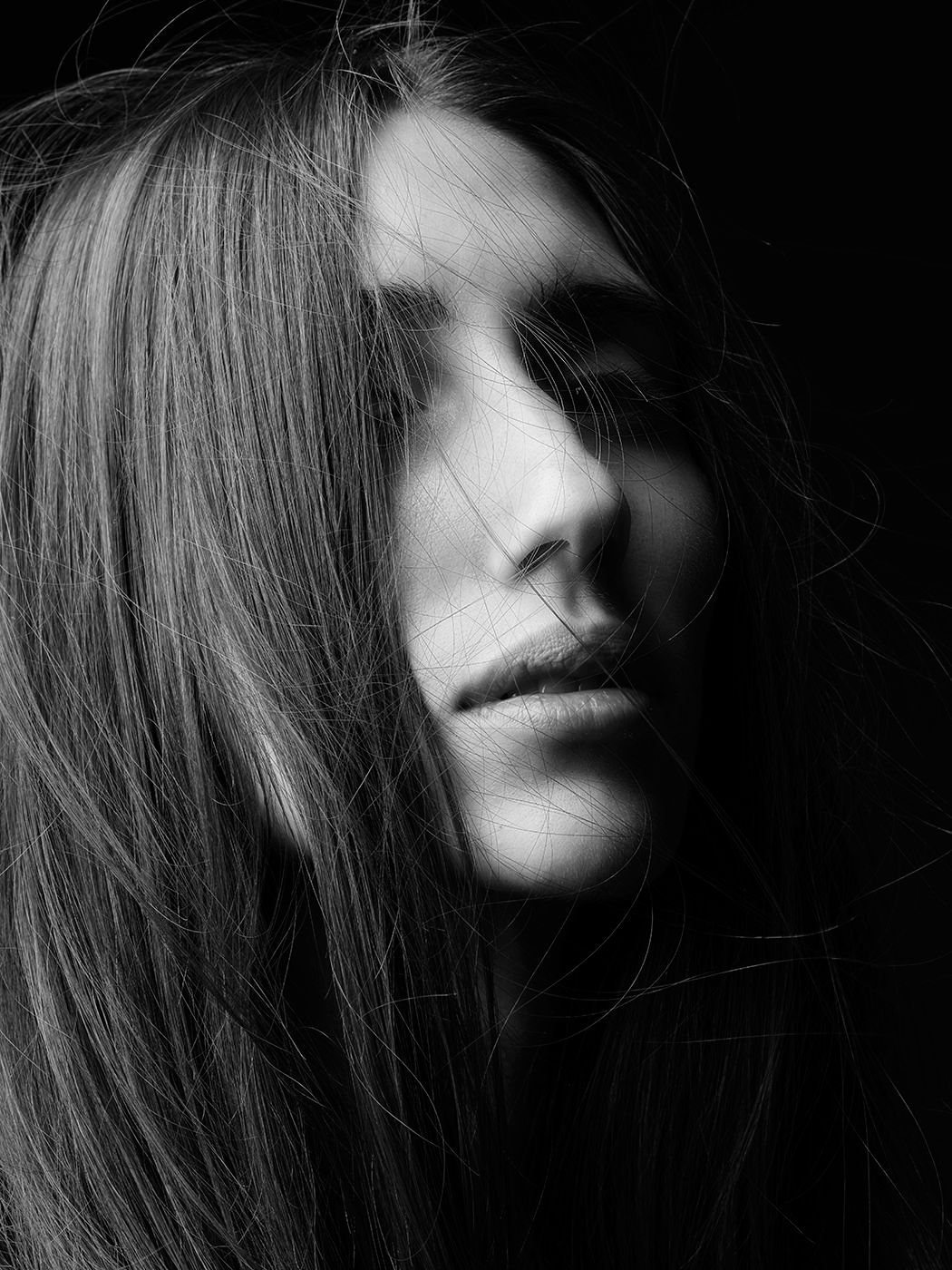 Black and white portrait of a young woman with long hair partially covering her face against a dark background.