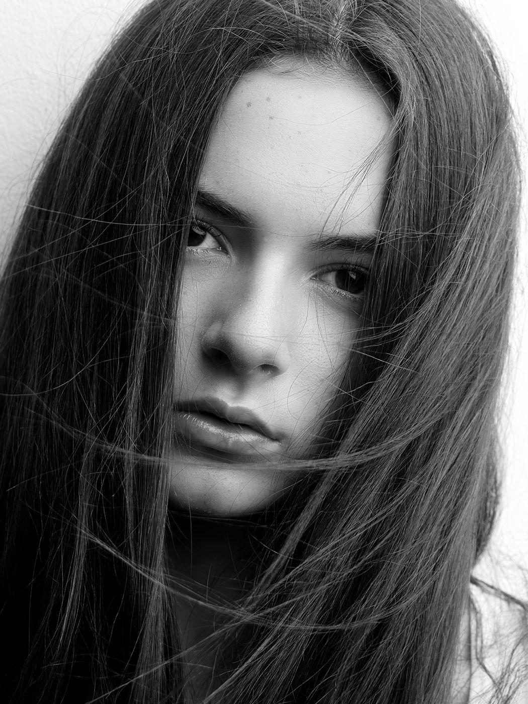 Black and white portrait of a young woman with long dark hair partially covering her face, intense gaze.