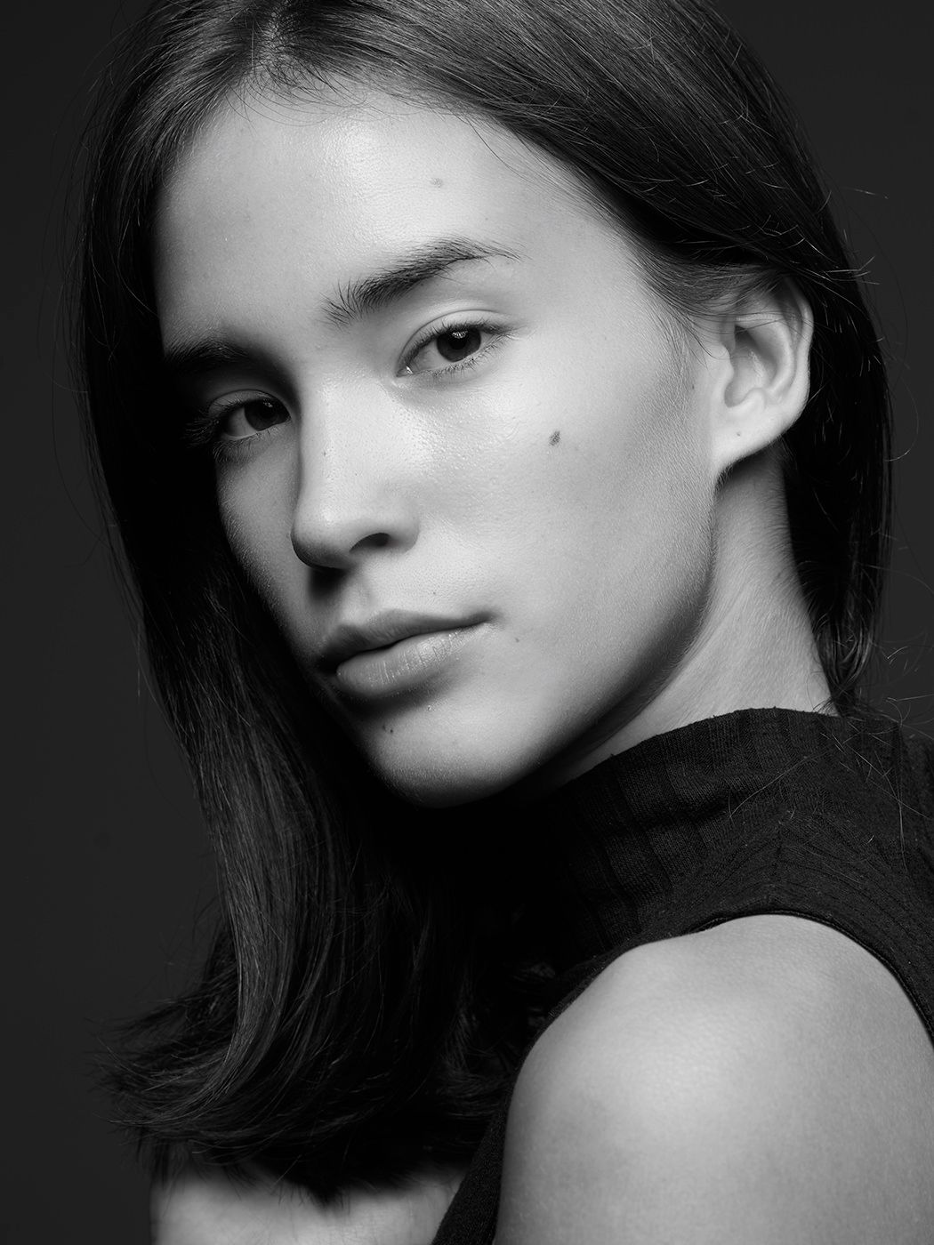 Black and white portrait of a young woman with dark hair wearing a black top, looking over her shoulder.