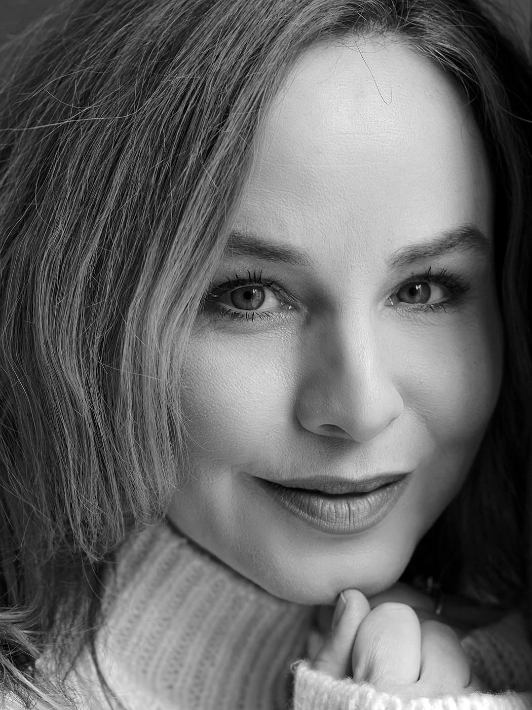 Black and white close-up portrait of a smiling woman with light eyes and soft features.