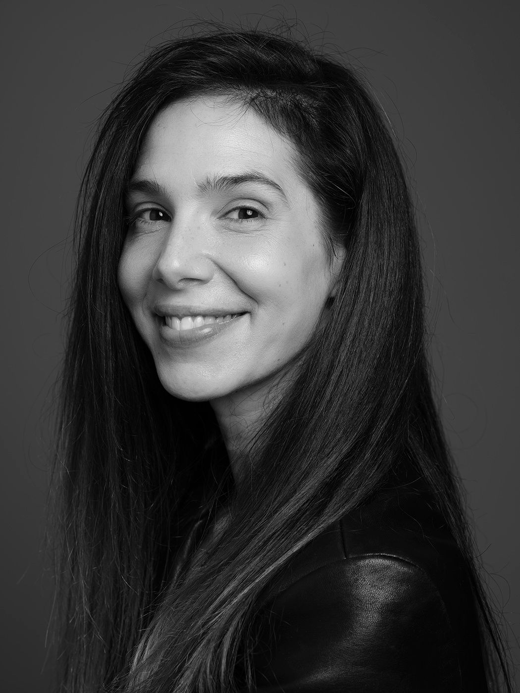 Black and white portrait of a smiling woman with long dark hair wearing a leather jacket.