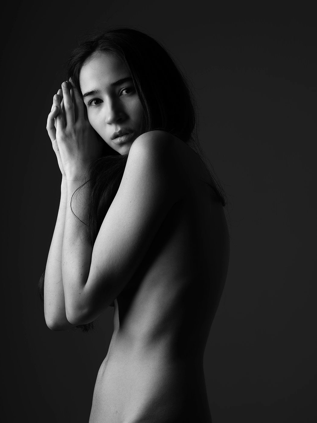 Black and white artistic portrait of a woman in profile, hand raised near face, dramatic studio lighting.