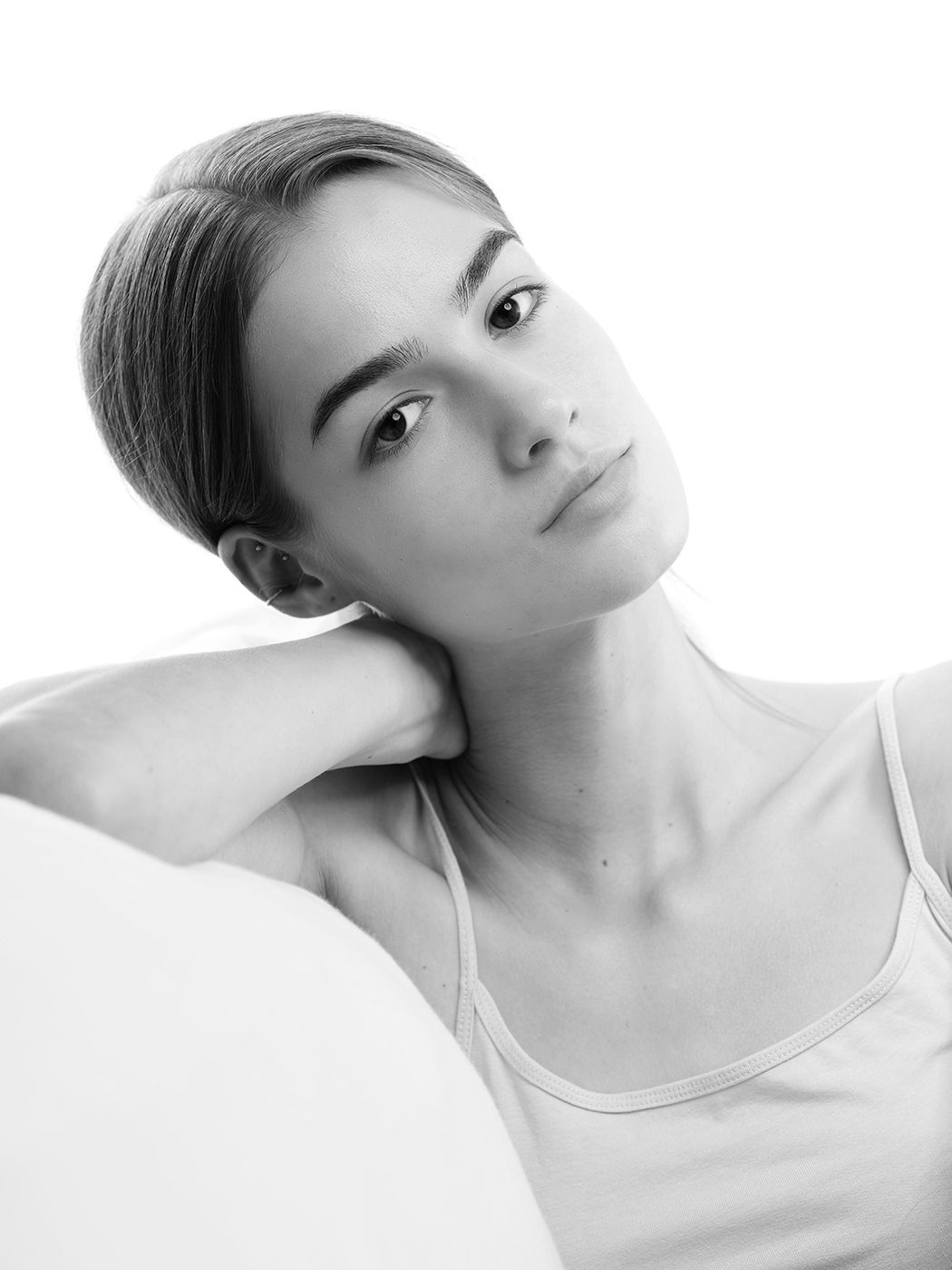 Black and white portrait of a young woman with slicked-back hair, hand on neck, wearing a tank top.