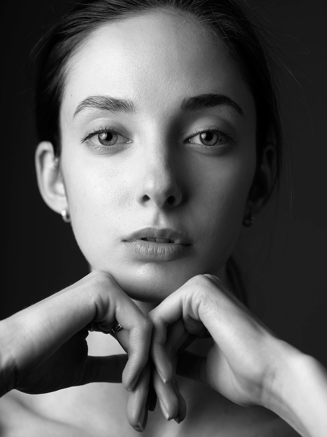 Black and white portrait of a young woman with hands clasped under chin, gazing directly at camera.
