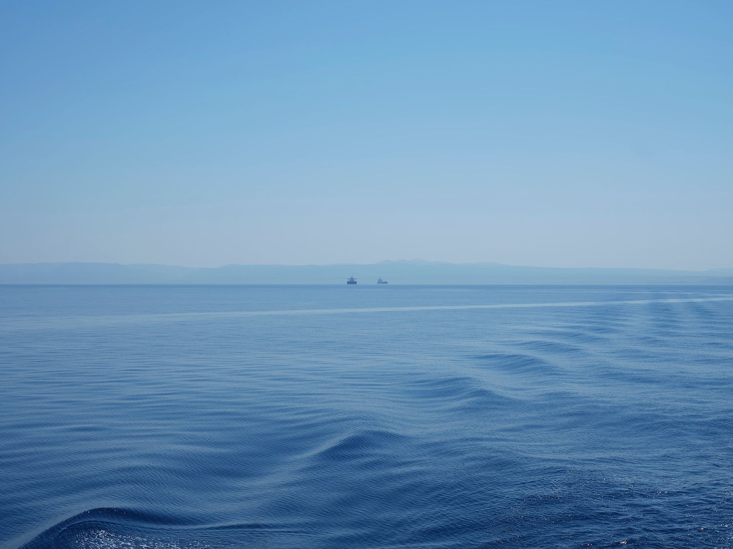 Calm blue ocean with gentle waves and a distant ship on the horizon under a clear sky.