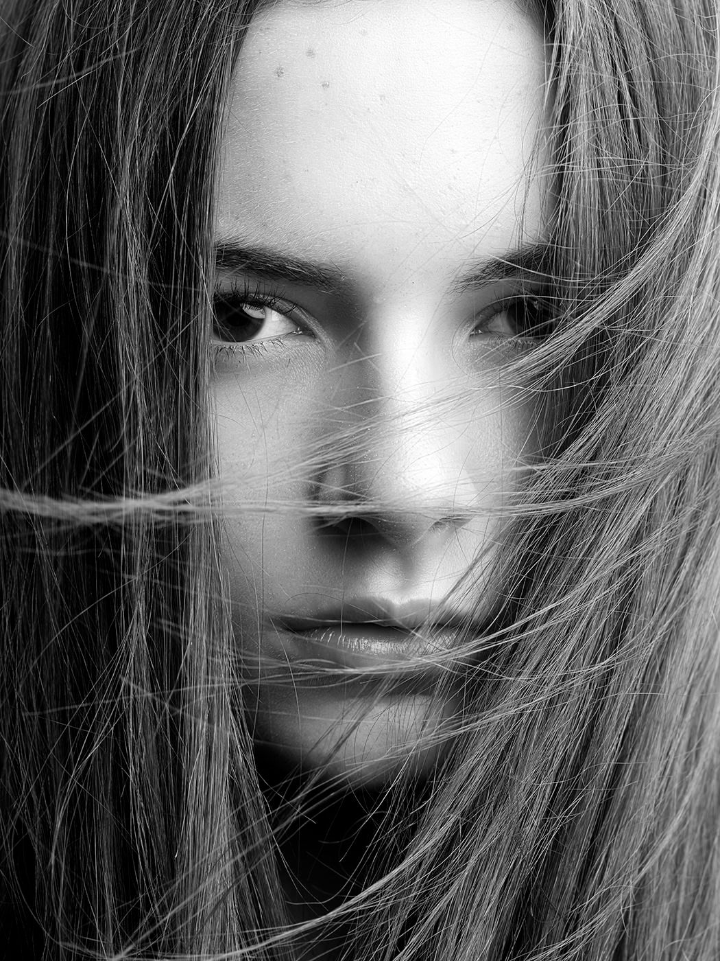 Black and white close-up portrait of a young woman with windswept hair partially covering her face.
