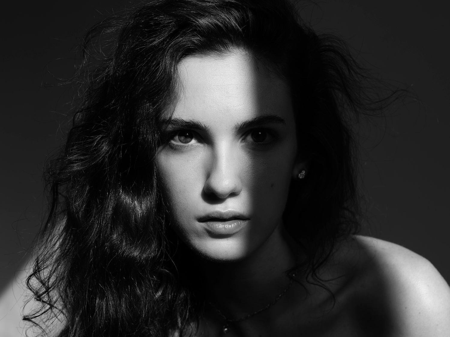 Black and white portrait of a young woman with long dark wavy hair and a serious expression.