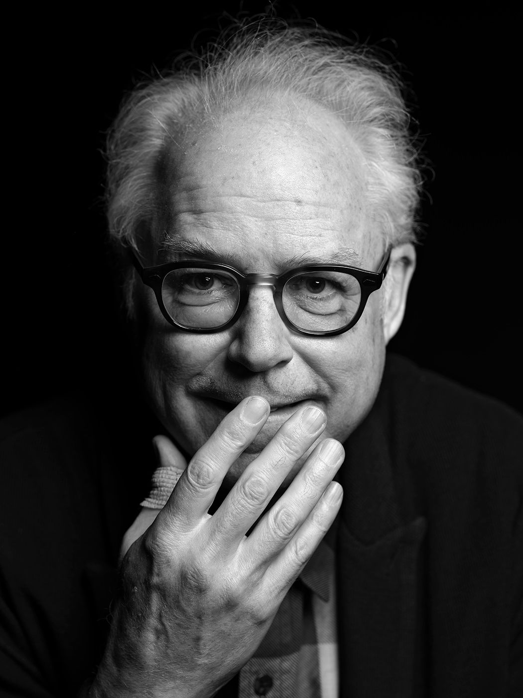 Black and white portrait of an older man with glasses, hand raised to his chin in a thoughtful pose. Bill Frisell