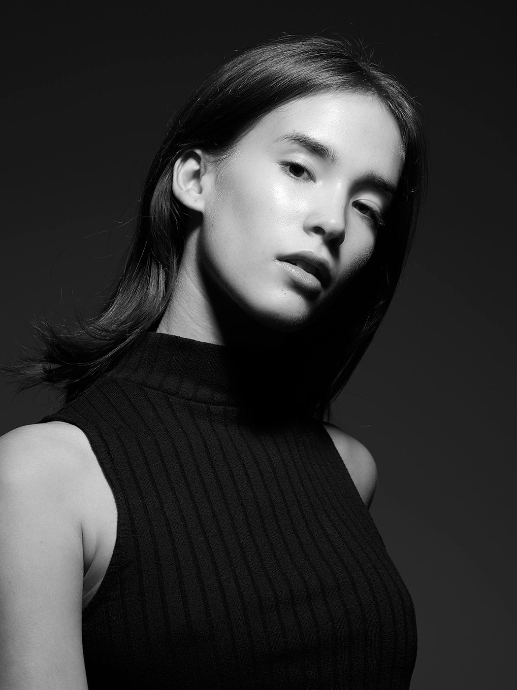 Black and white portrait of a young woman in a black ribbed sleeveless top, with dark hair and a subtle gaze.