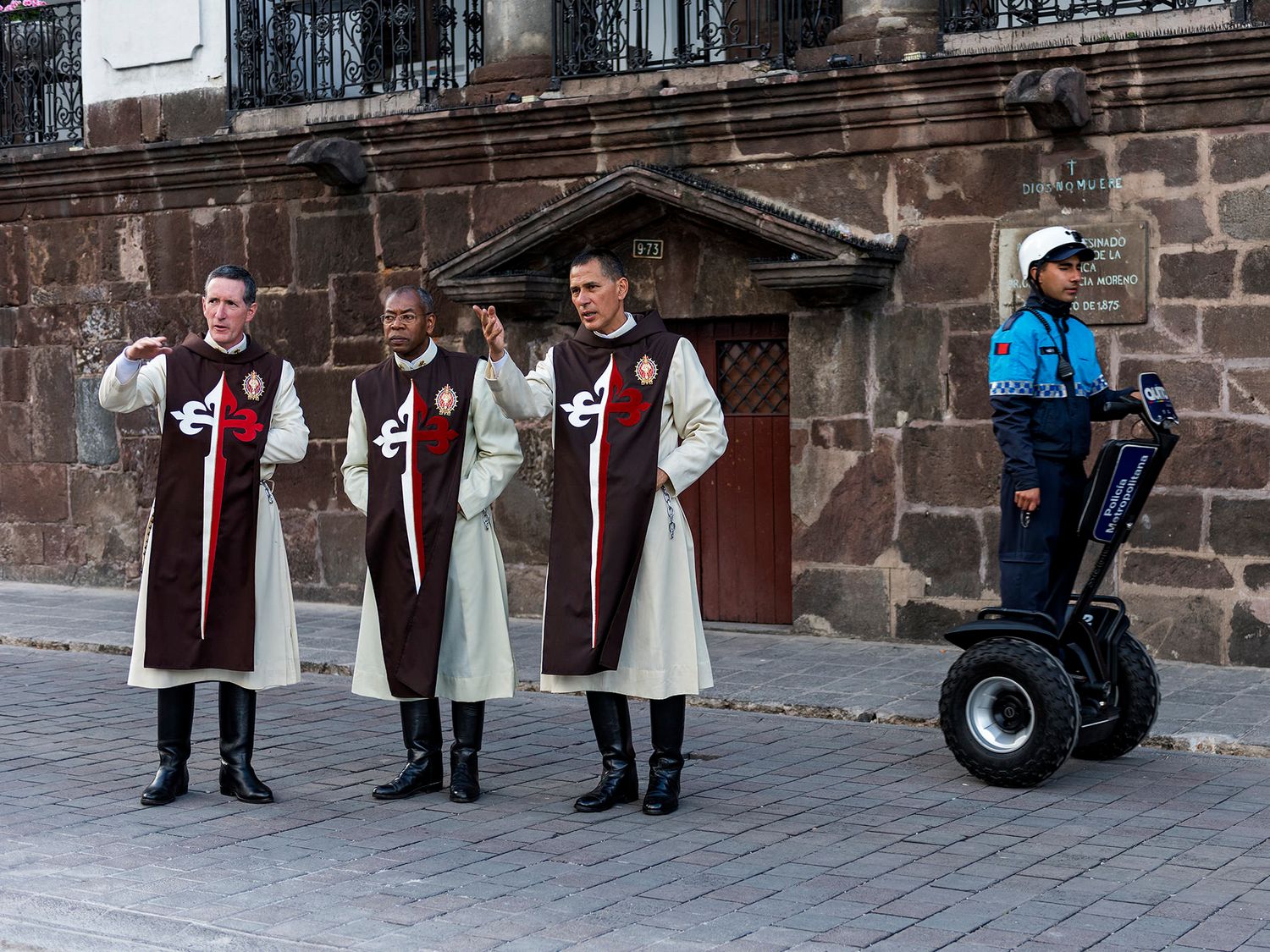 Three clergy members in robes stand beside a police officer on a Segway outside a historic stone building.