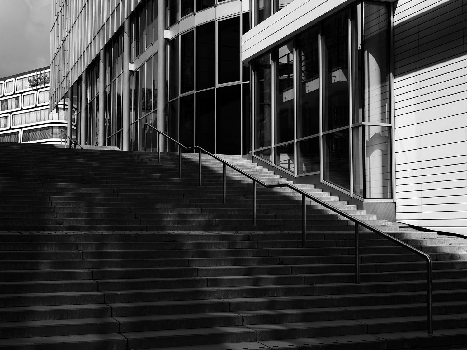 Black and white image of wide concrete steps with metal railings leading to a modern building entrance.
