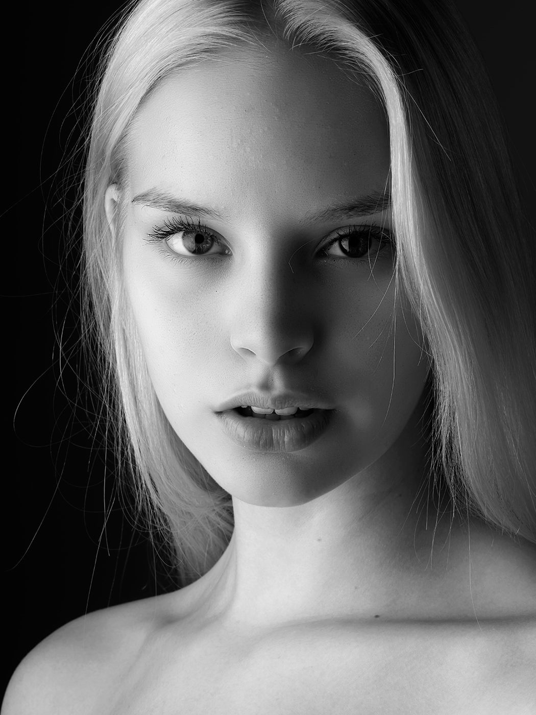 Black and white portrait of a young woman with long blonde hair and striking features against a dark background.