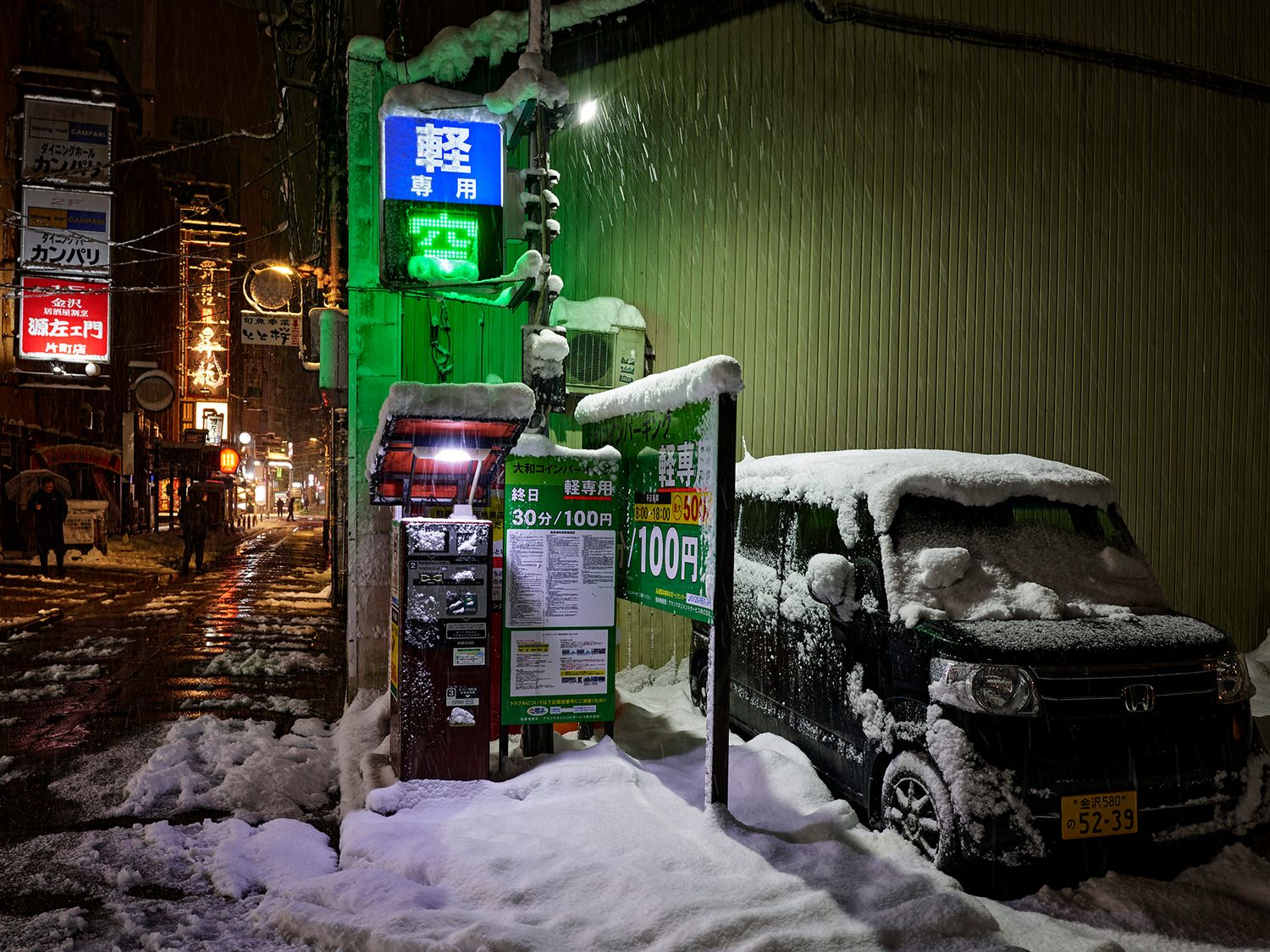 Snowy night street scene in Japan with a snow-covered van, vending machine, and illuminated signs in a winter storm.
