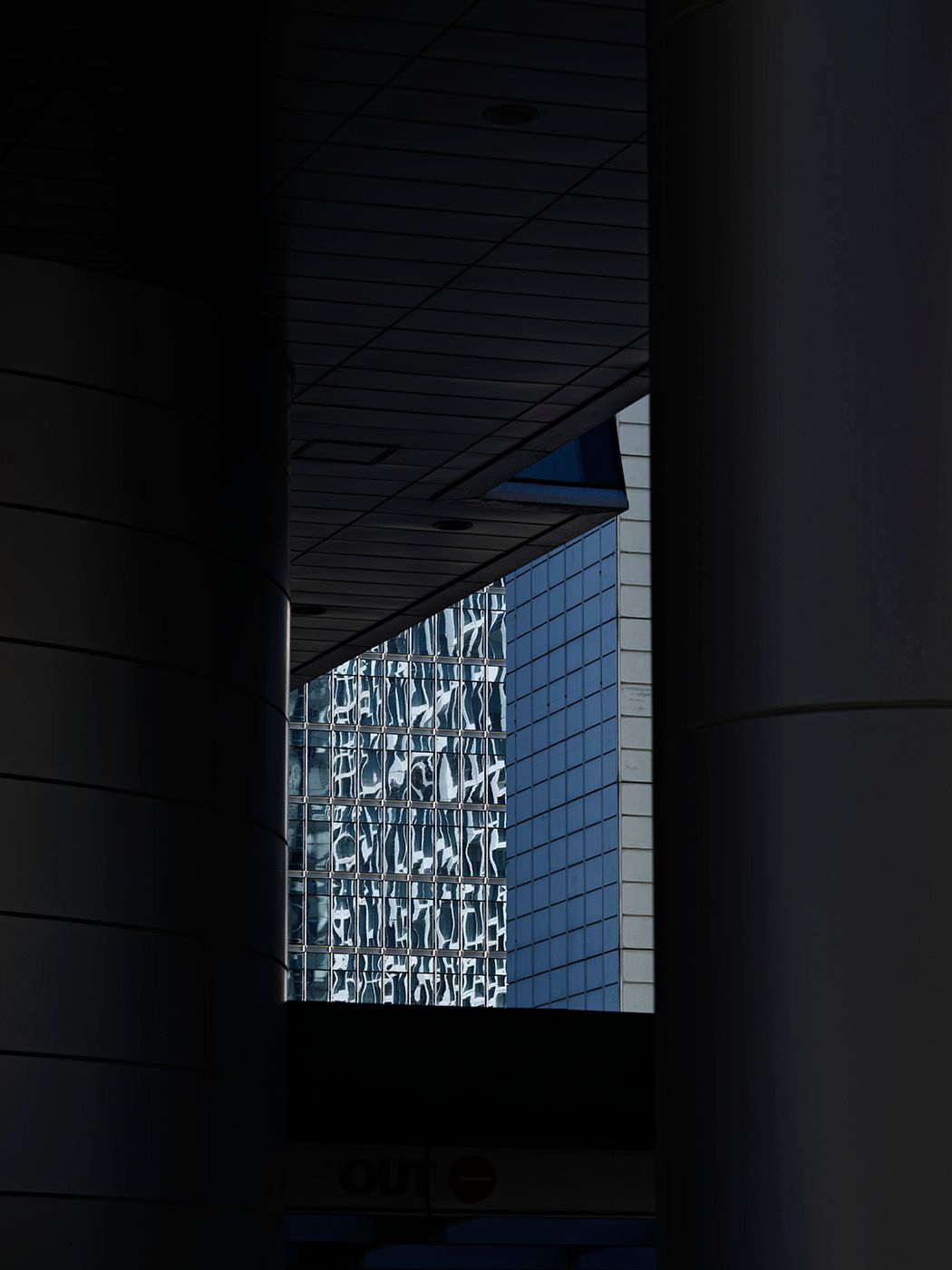Dark architectural framing reveals a sunlit building facade with decorative glass panel art between shadowed columns.