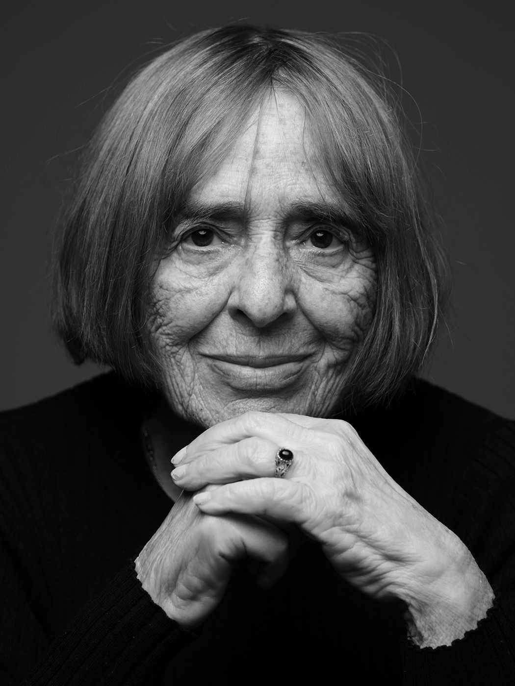 Black and white portrait of a smiling elderly woman with short gray hair and clasped hands.
