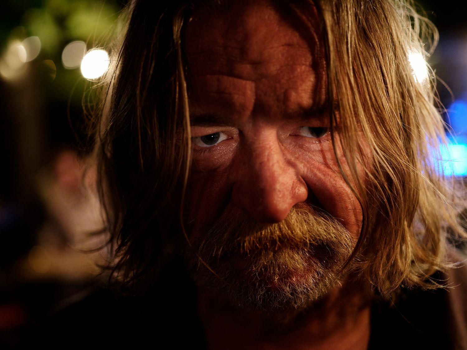 Close-up of an older man with long hair and beard in dramatic night lighting.
