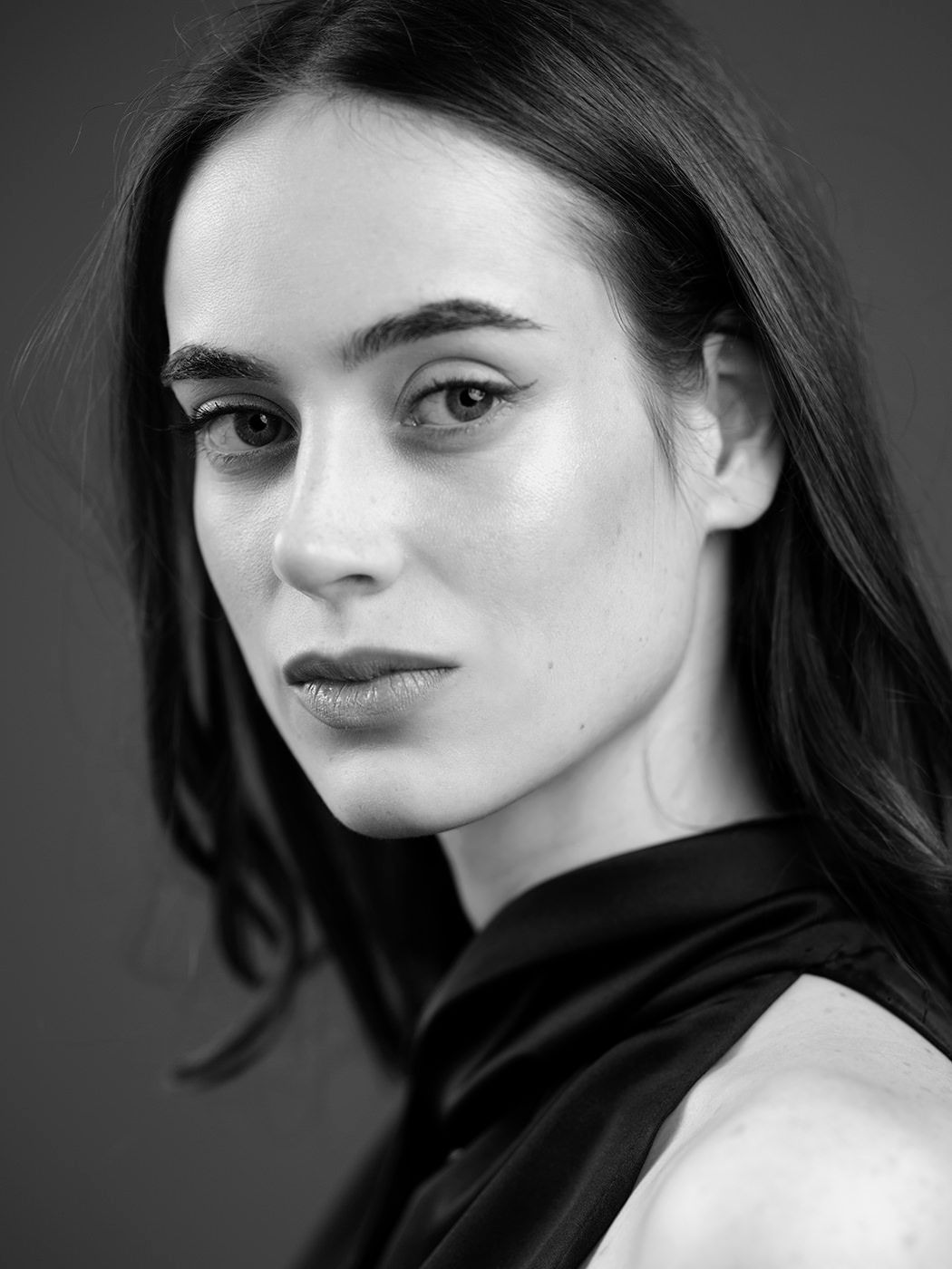 Black and white studio portrait of a young woman with long dark hair wearing a black top.