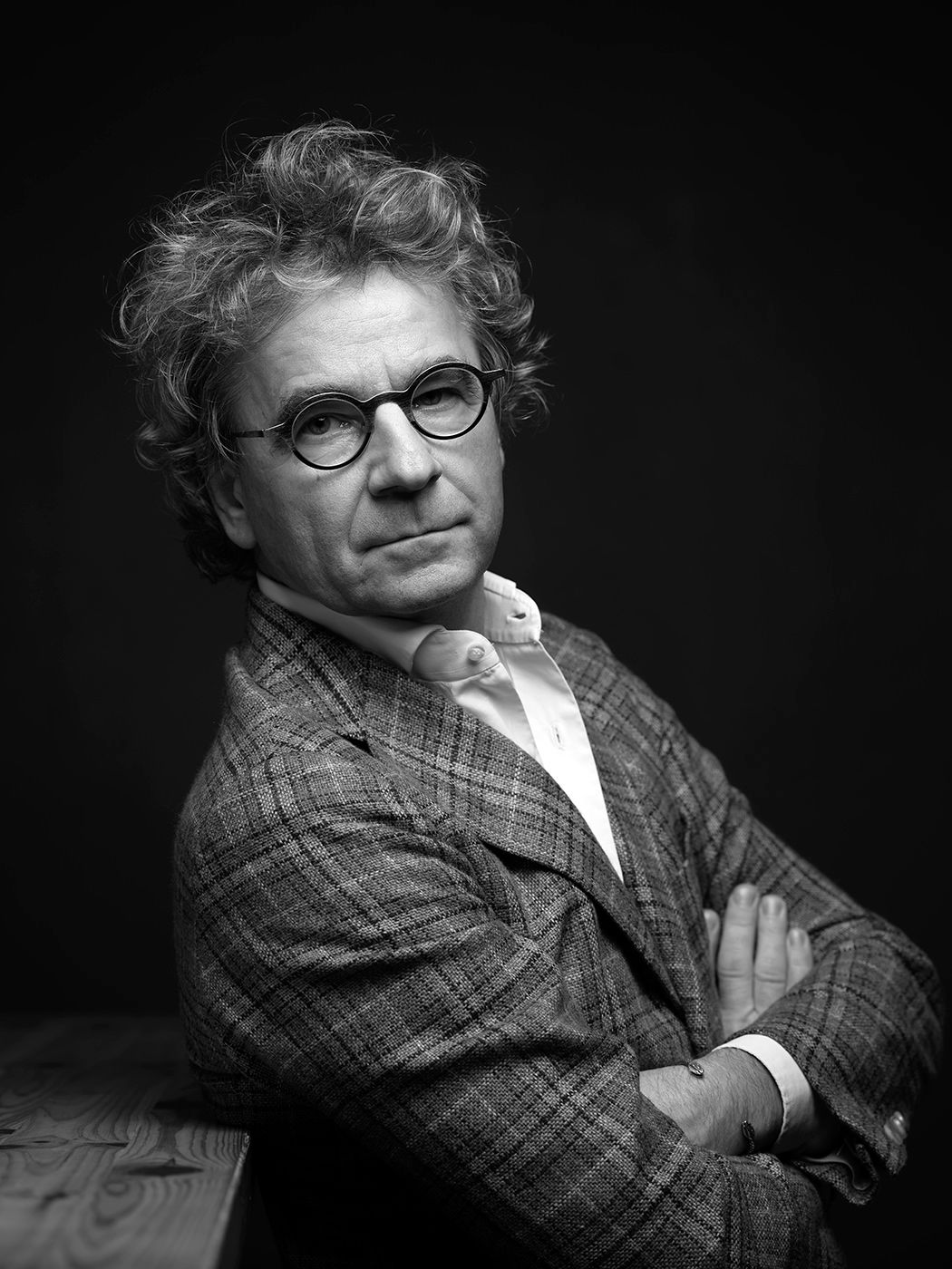 Black and white portrait of a middle-aged man with curly hair and round glasses, arms crossed, wearing a plaid blazer.