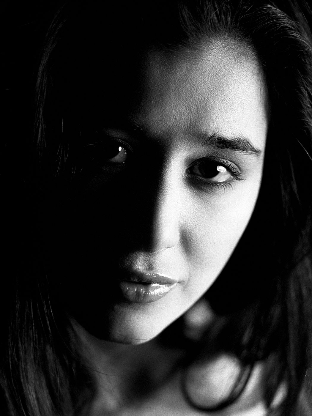 High contrast black and white portrait of a young woman with dark hair, half face in shadow.