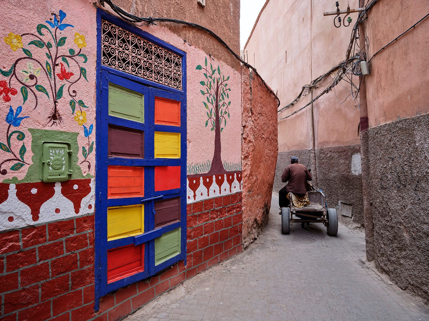 Colorful painted wall with vibrant window shutters in a narrow Marrakech medina alley, Morocco.
