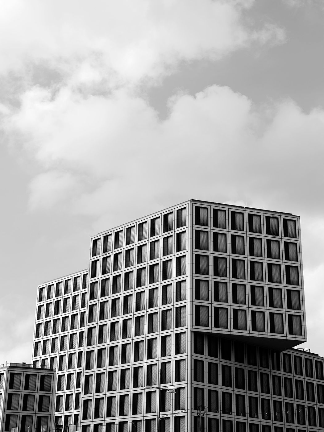 Black and white photo of modern geometric office buildings with grid-like windows against a cloudy sky.