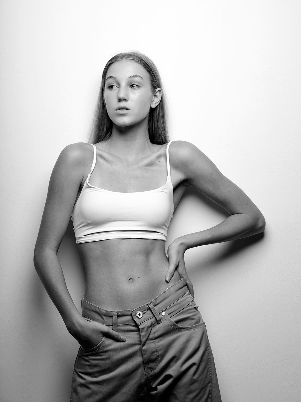 Black and white studio portrait of a young woman in a crop top and jeans posing confidently.