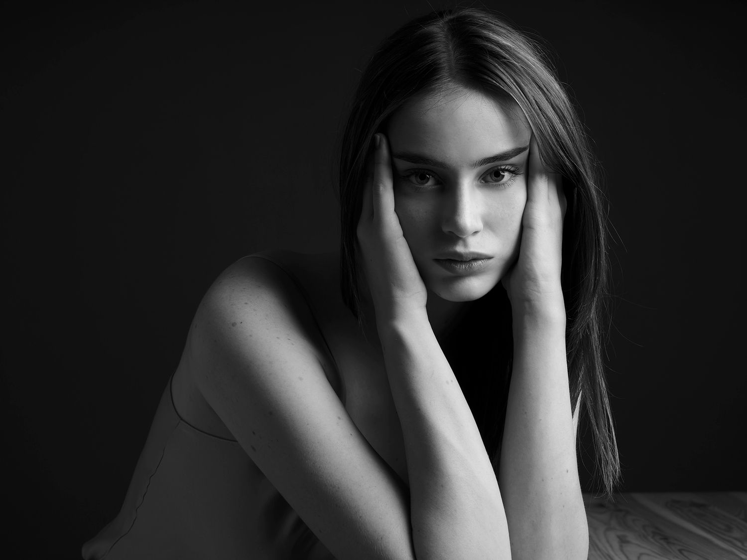 Black and white portrait of a young woman with long hair, hands framing her face, pensive expression.