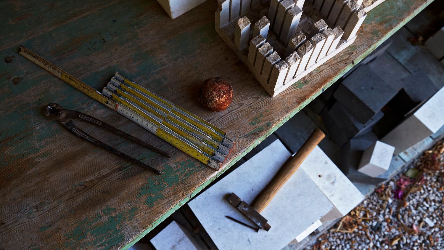 Rustic workbench with hammer, measuring tape, bolt cutters, and stacked blocks on a weathered green surface.