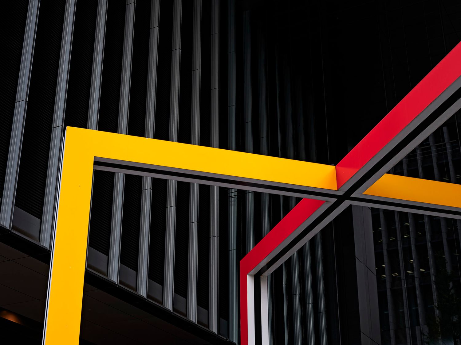 Abstract architectural detail featuring bold yellow and red geometric lines against dark metal railings.