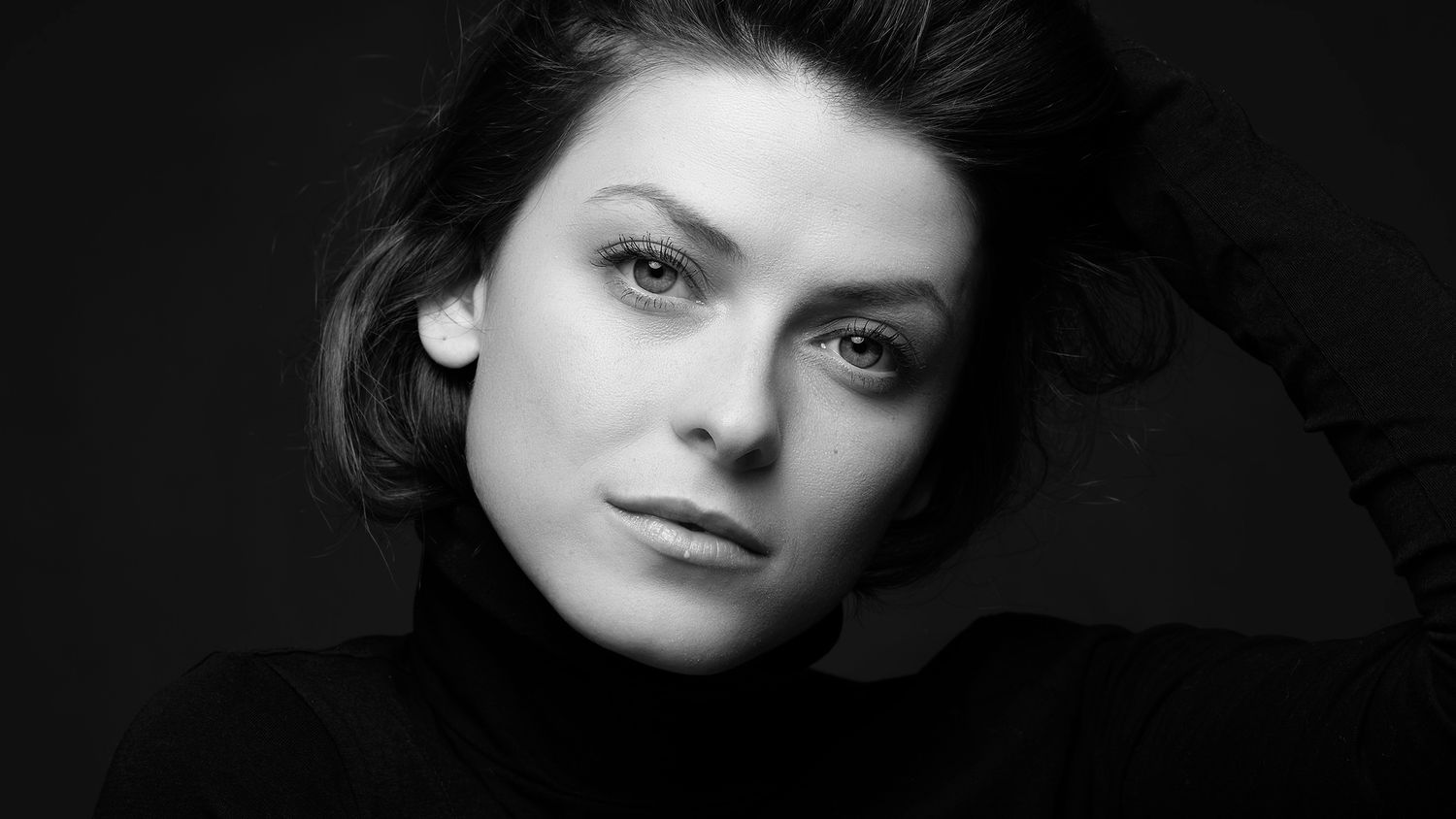 A striking black and white close-up portrait of a young woman with dark hair and light eyes.
