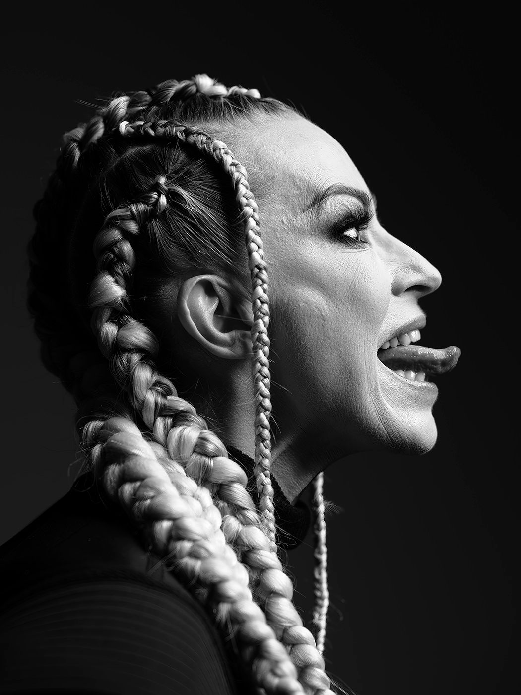Black and white profile portrait of a woman with long braided hair, mouth open, dramatic studio lighting. Pásztor Anna