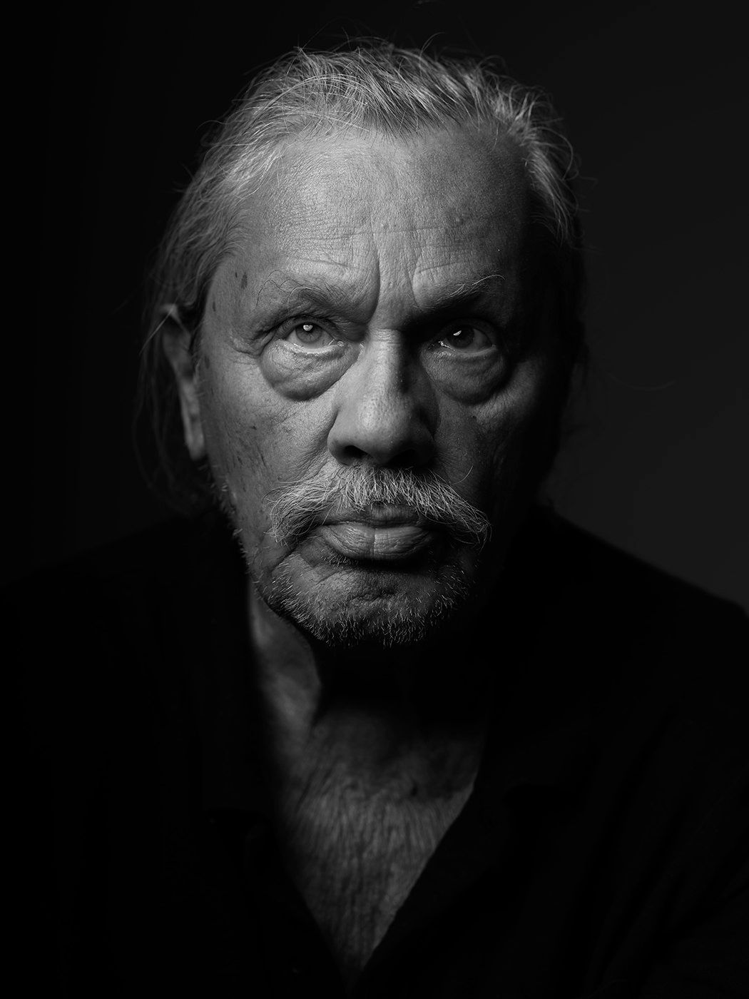 Black and white portrait of an elderly man with gray hair, mustache, and intense gaze in dramatic lighting. Ráduly Mihály, musician