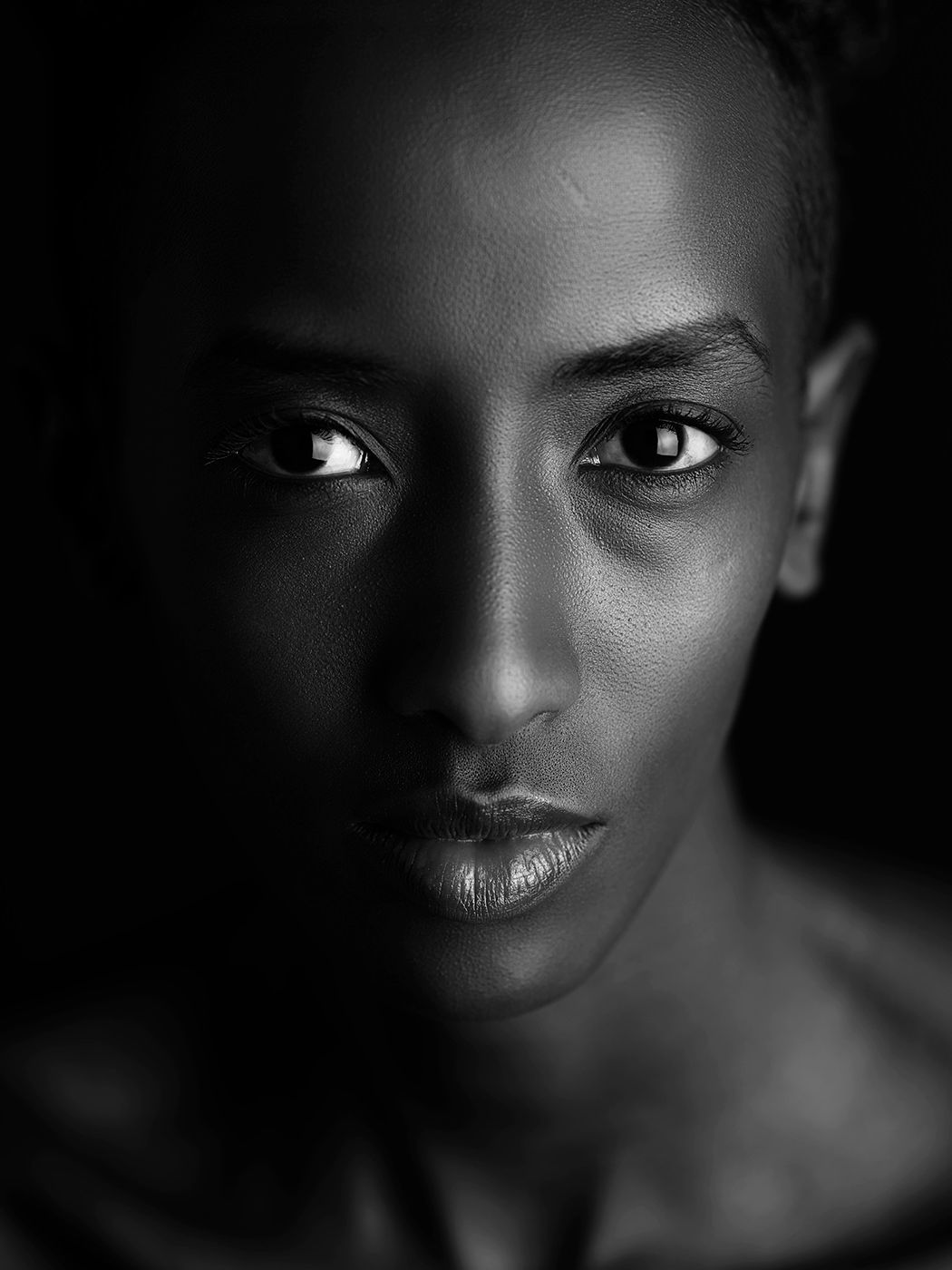 Black and white portrait of a woman with short hair, gazing intensely at the camera in dramatic lighting.