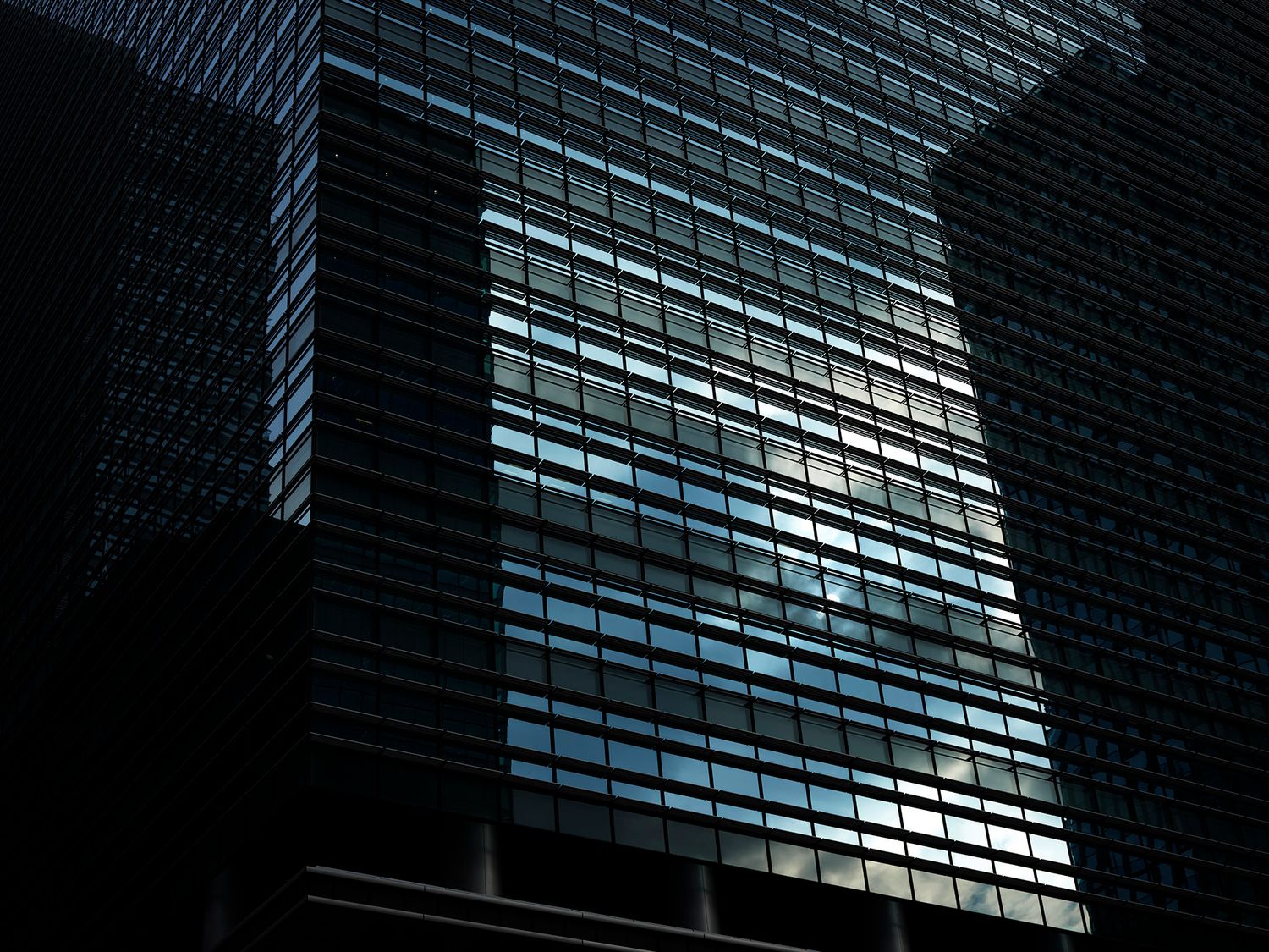 Dramatic glass skyscraper facade reflecting blue light against dark urban sky.