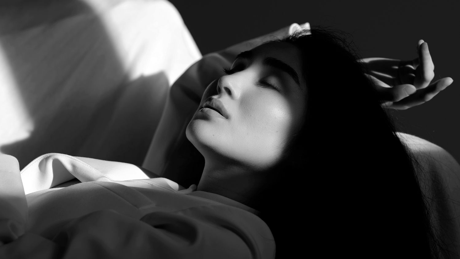 A woman with dark hair lies back with eyes closed in a dramatic black and white portrait.