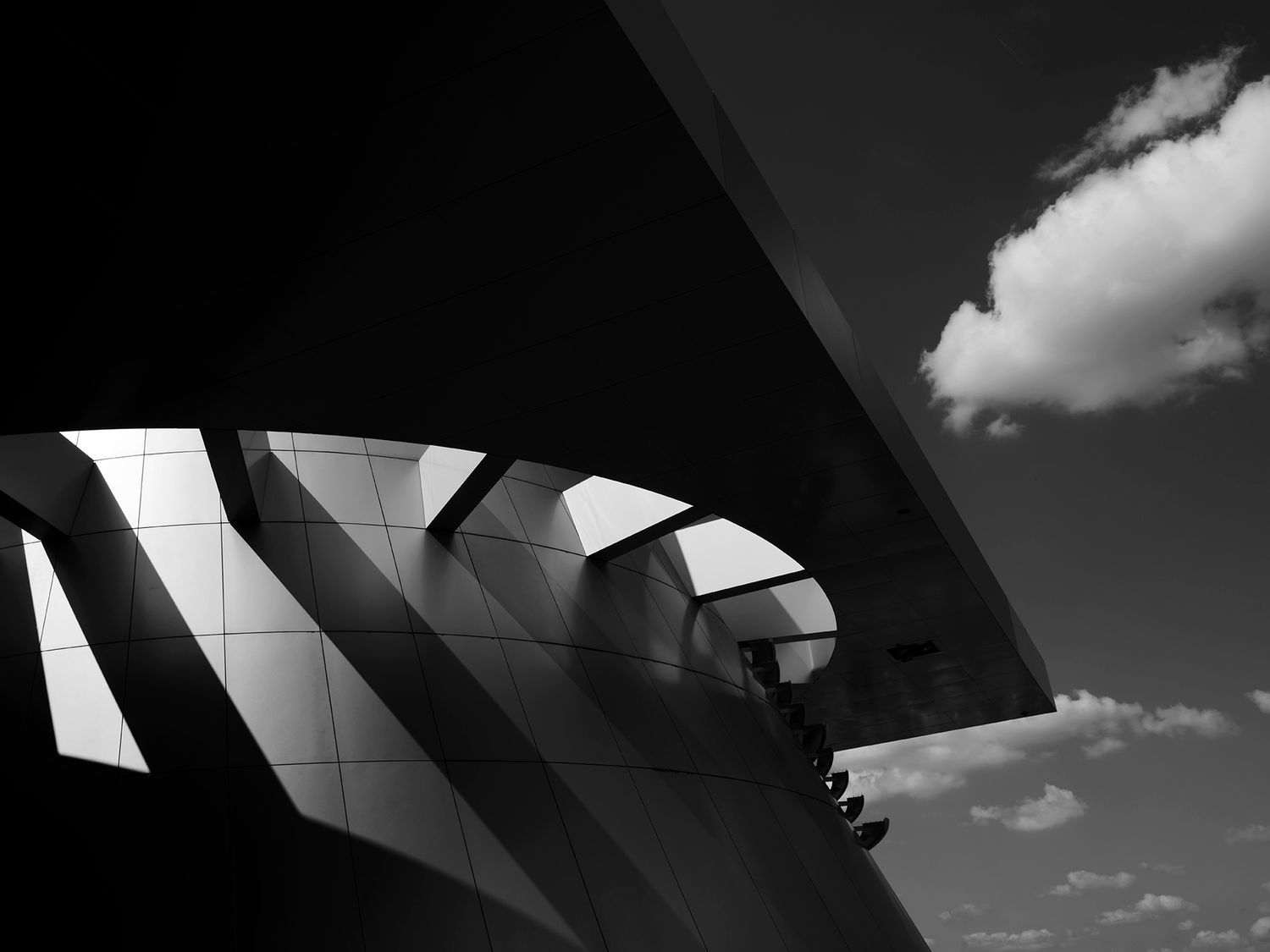 Black and white architectural photography of curved modern building details against a cloudy sky.