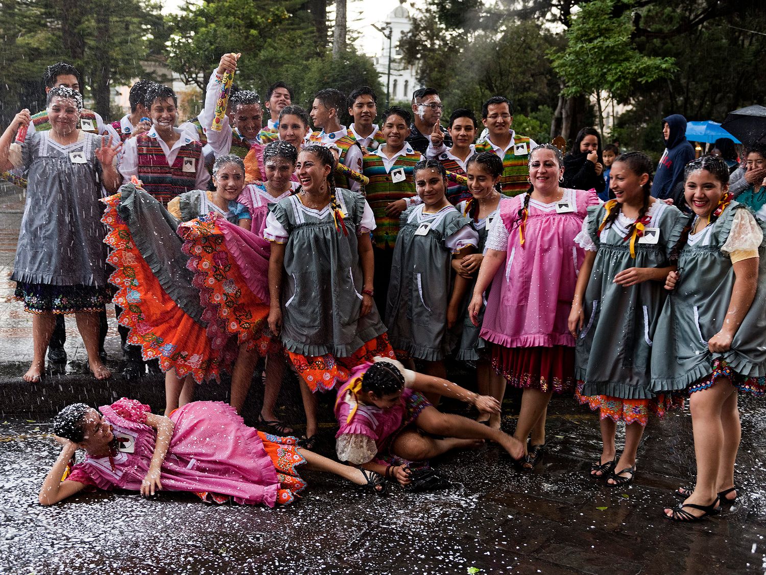 Group of women in colorful traditional dresses posing joyfully in the rain during a festive cultural celebration.