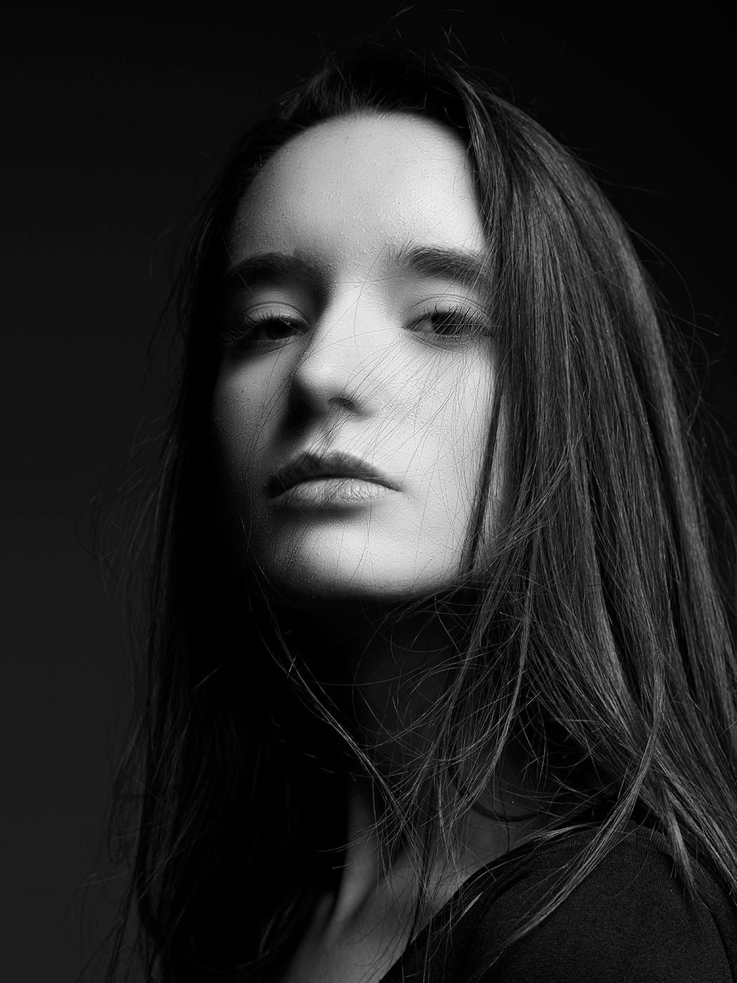 Black and white portrait of a young woman with long dark hair, dramatic lighting, moody studio photography.